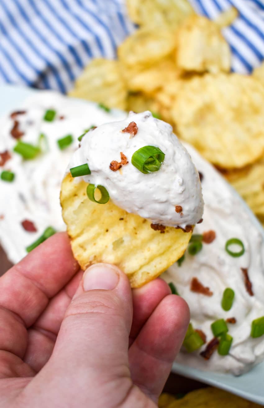 a hand holding up a potato chip topped with creamy bacon horseradish dip