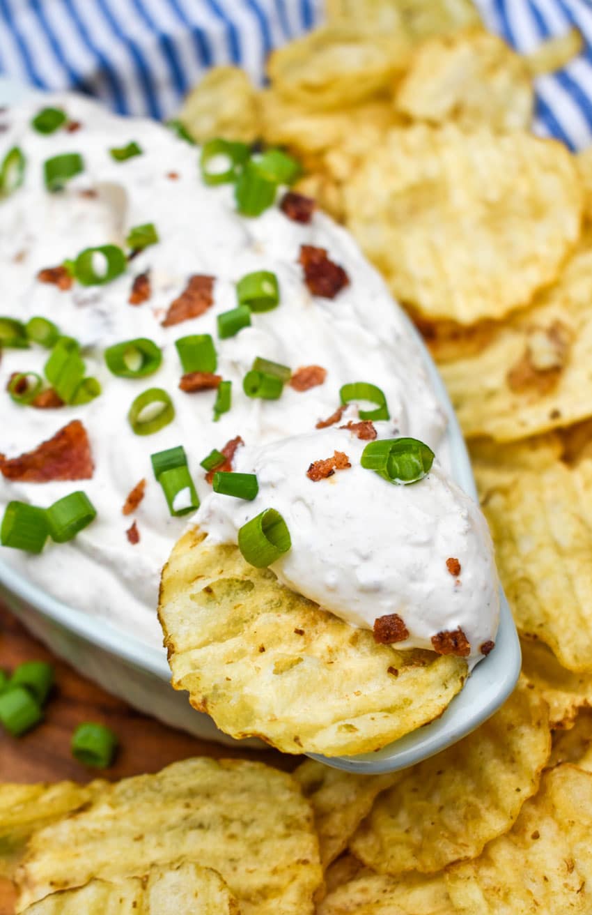 a dish of creamy bacon horseradish dip with a potato chip stuck in the middle