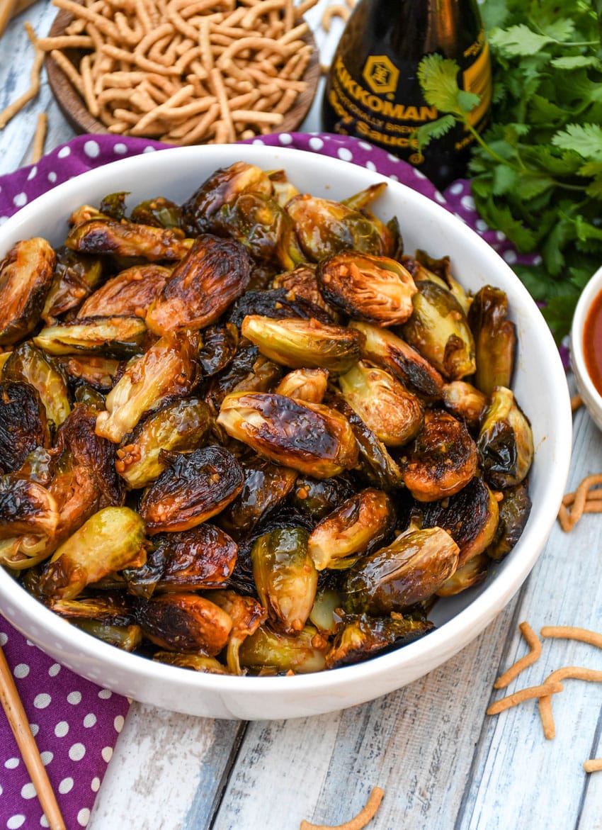 crispy soy glazed brussels sprouts in a white serving bowl with wooden chop sticks on the side