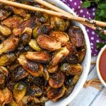 crispy soy glazed brussels sprouts in a white serving bowl with wooden chop sticks on the side