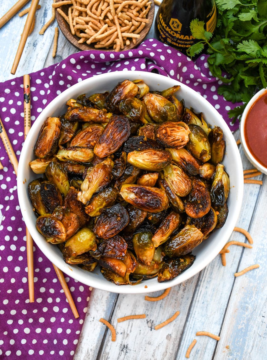 crispy soy glazed brussels sprouts in a white serving bowl with wooden chop sticks on the side
