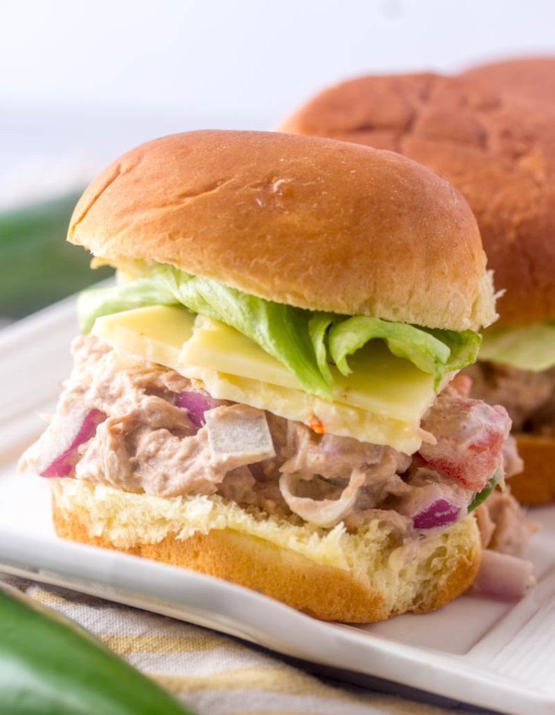 a close up of a single Spicy Tuna Salad Sandwich slider, you can see lettuce and sliced cheese with the tuna salad piled high inside a fluffy bun