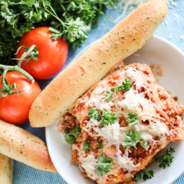 a slice of crockpot lasagna served on a white plate with freshly baked breadstick