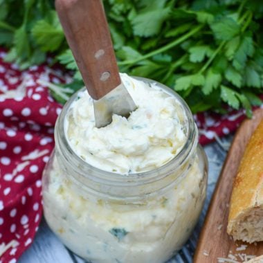 Italian garlic infused butter spread over sliced Italian bread on a wooden cutting board