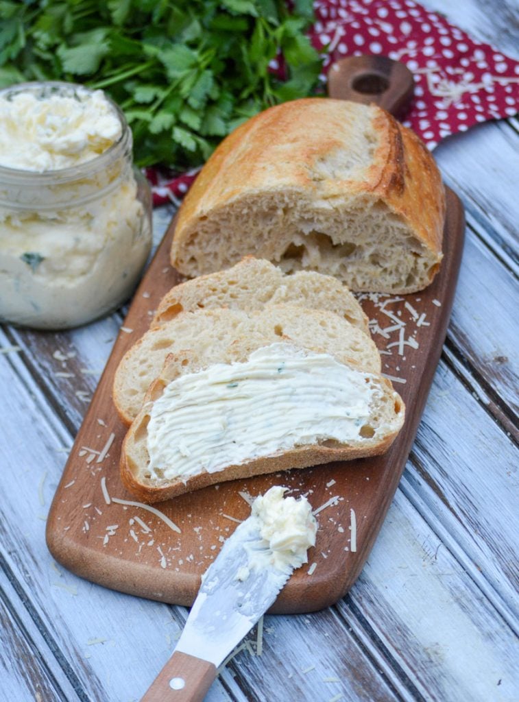 Italian garlic infused butter spread over sliced Italian bread on a wooden cutting board