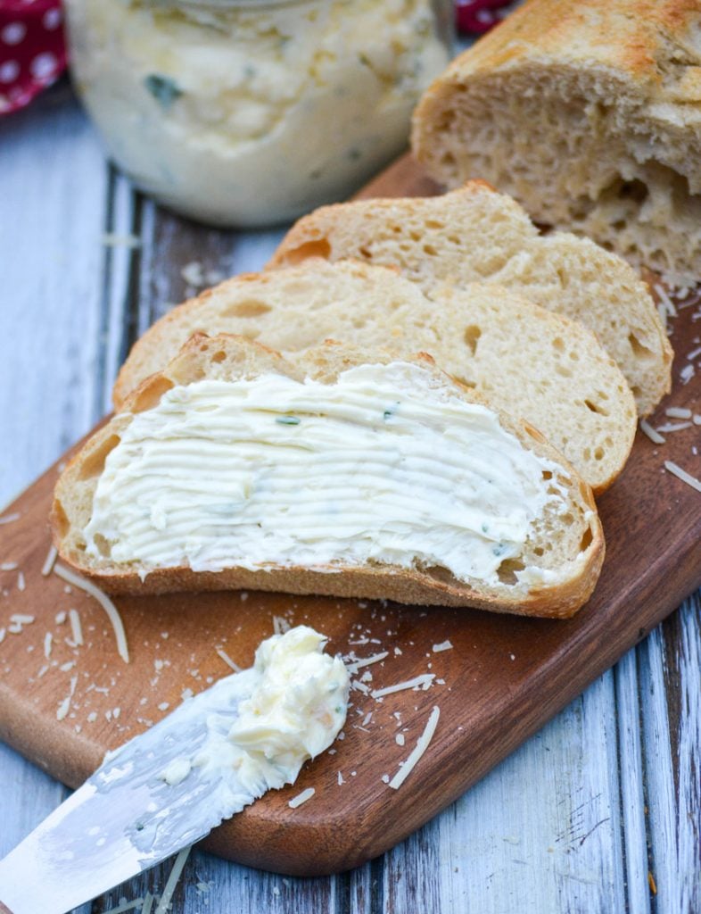 Italian garlic infused butter spread over sliced Italian bread on a wooden cutting board