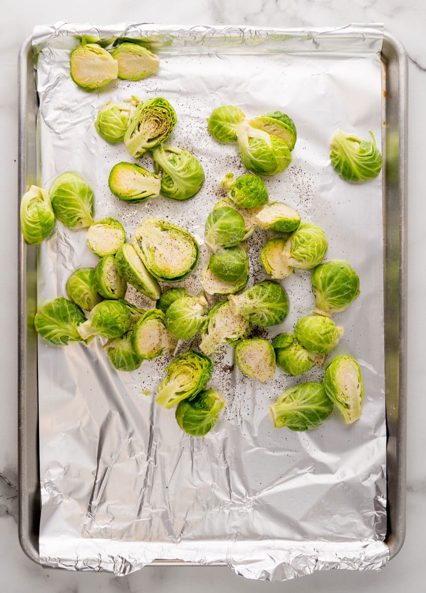 clean halved brussels sprouts spread out on an aluminum foil lined baking pan