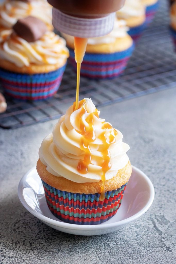 a bottle shown adding a rich caramel drizzle to a Baby Ruth Cupcake