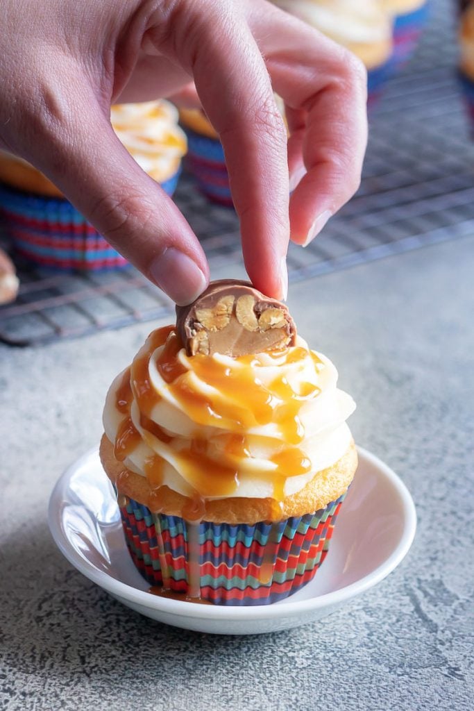 a hand shown topping a baby ruth cupcake with a piece of candy bar