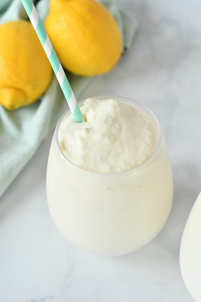 dole whip shown in a glass with a colorful straw and fresh lemons in the background