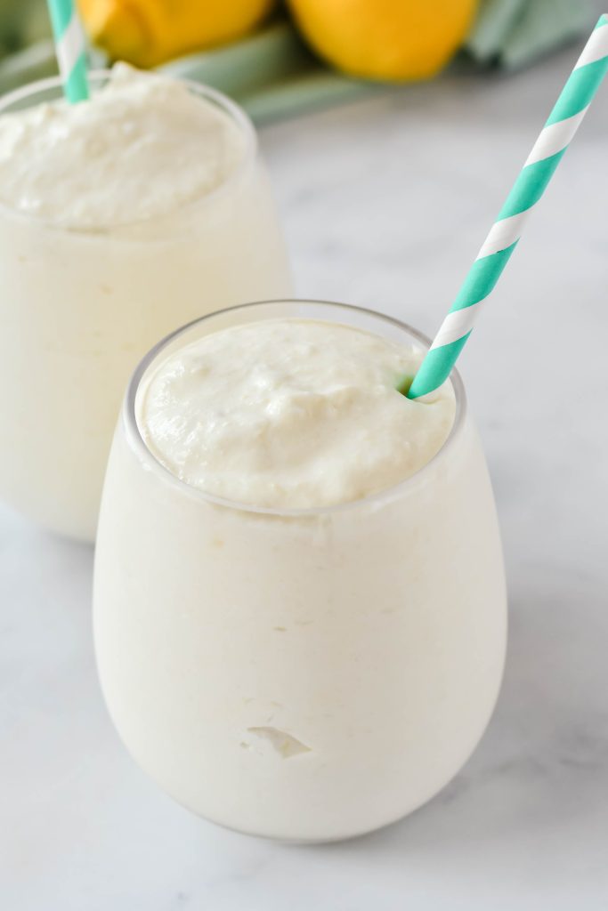 frozen dole whip shown in a glass with a colorful straw and fresh lemons in the background