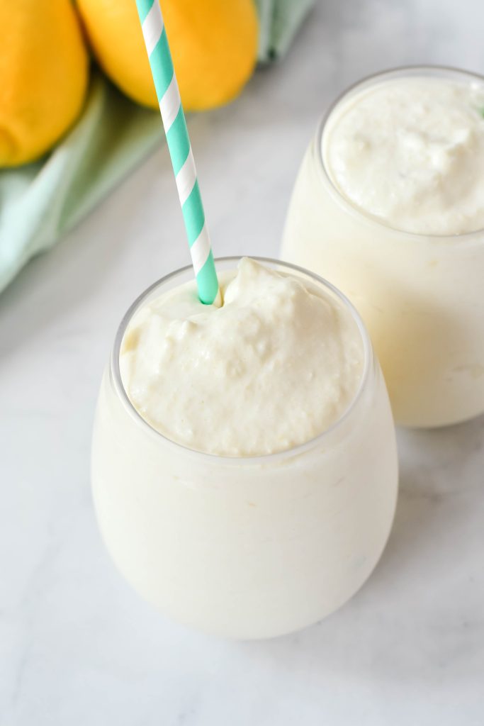 dole whip shown in a glass with a colorful straw and fresh lemons in the background