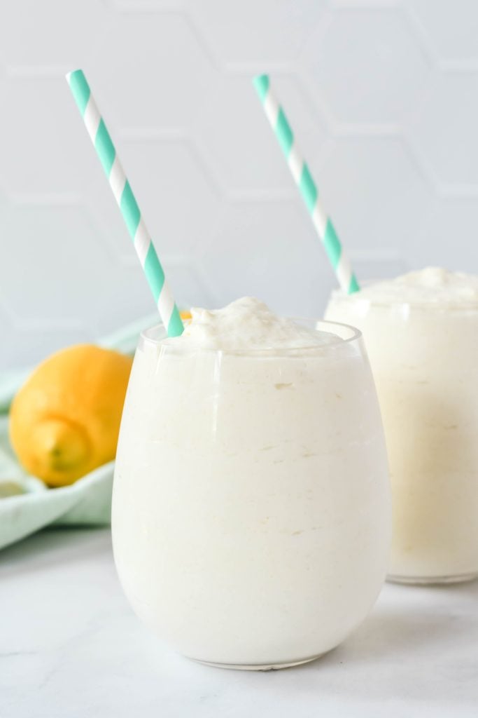 creamy frozen dole whips shown in a glass with a colorful straw and fresh lemons in the background