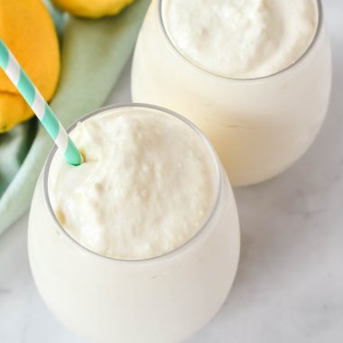 creamy frozen dole whips shown in a glass with a colorful straw and fresh lemons in the background