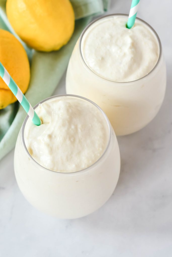 creamy frozen dole whips shown in a glass with a colorful straw and fresh lemons in the background