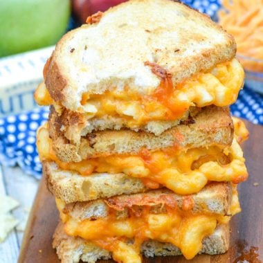 a stack of grilled mac and cheese sandwich halves on a wooden cutting board