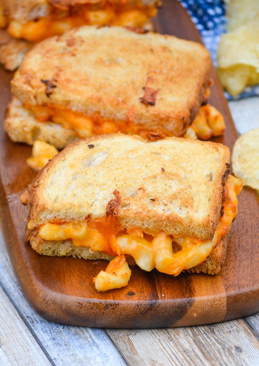 two grilled mac and cheese sandwiches arranged in a row on a narrow wooden cutting board