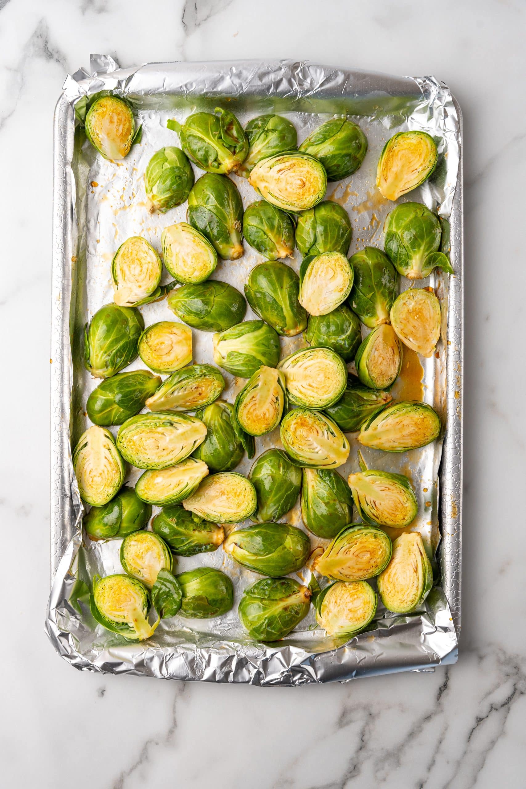 sauced brussels sprout halves on a foil lined baking tray