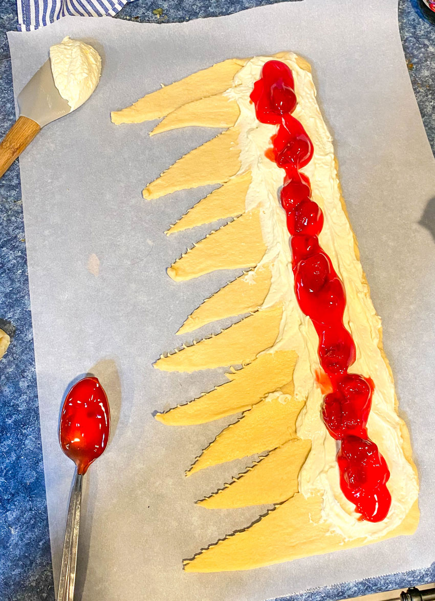 crescent roll dough arranged in a single line and spread with cheesecake filling and strawberry pie filling