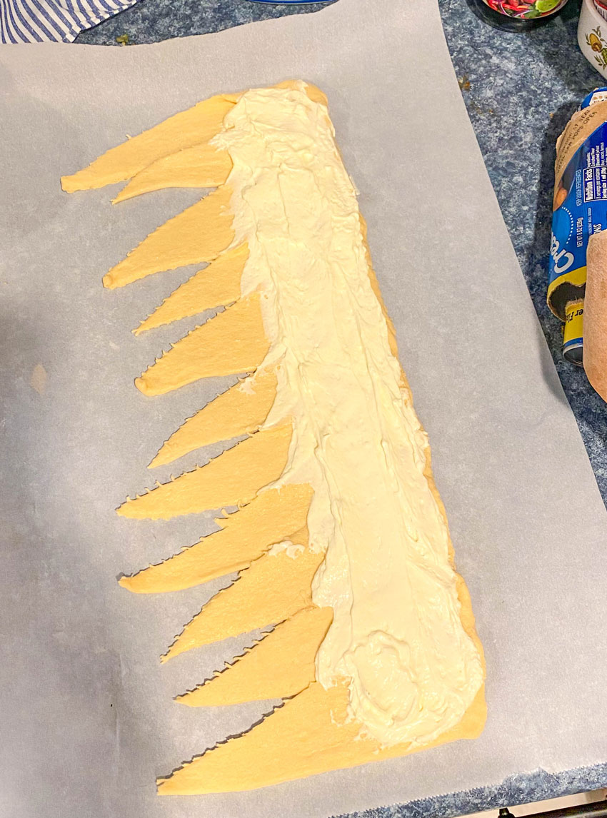 crescent roll dough arranged in a single line and spread with cheesecake filling