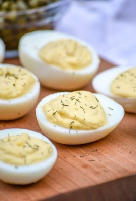 french style deviled eggs sprinkled with dried herbs and arranged on a wooden cutting board