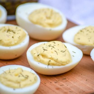 french style deviled eggs sprinkled with dried herbs and arranged on a wooden cutting board