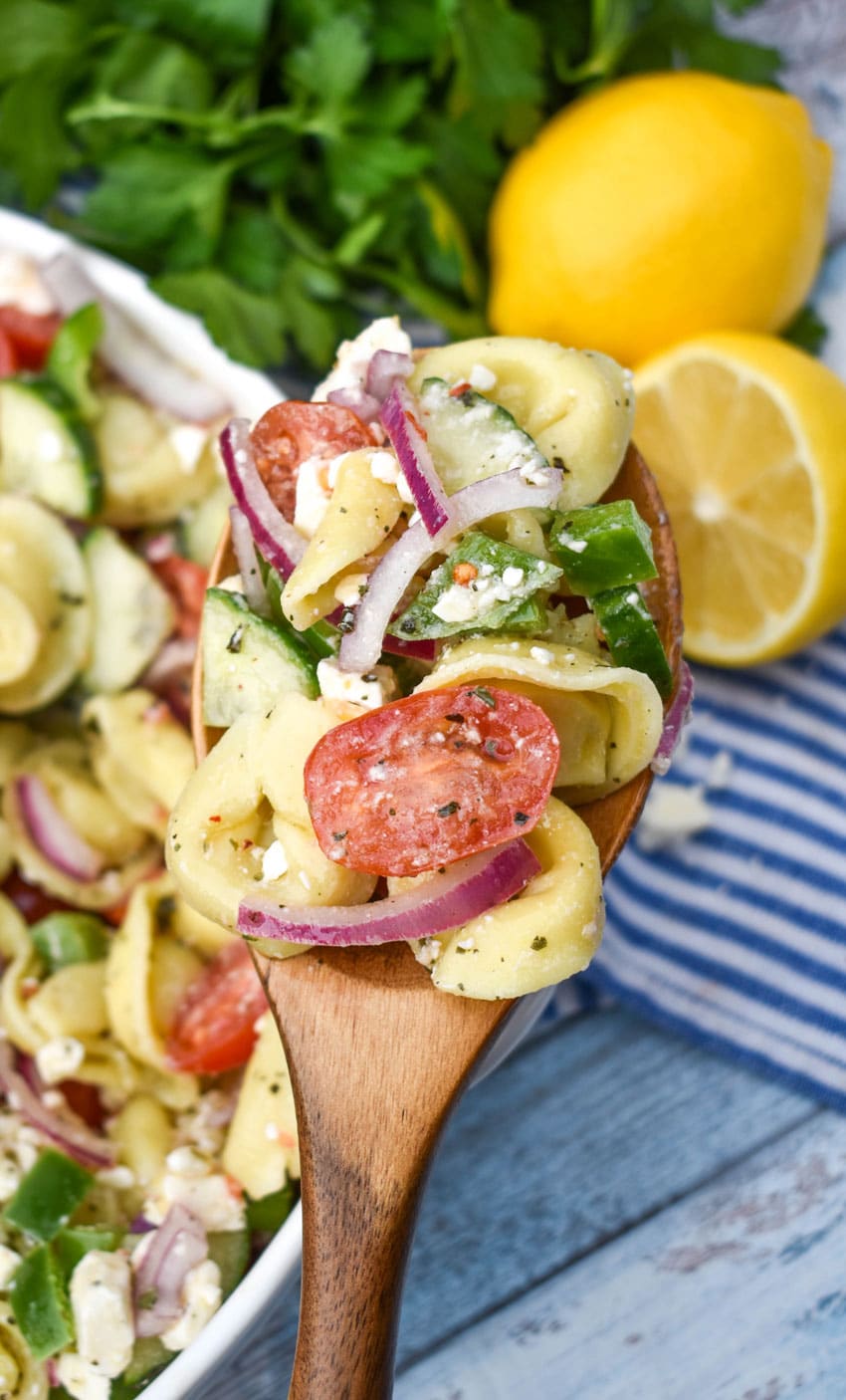 a wooden spoon holding up a scoop of mediterranean tortellini pasta salad