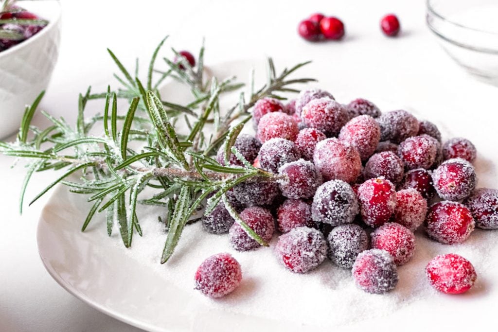 sugared cranberries and rosemary shown on a bed of white sugar