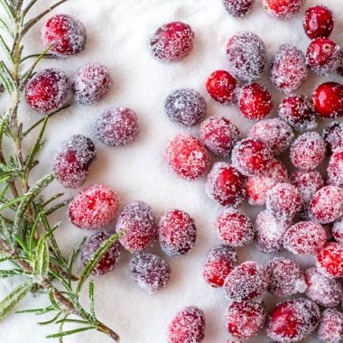 sugared cranberries and rosemary shown on a bed of white sugar
