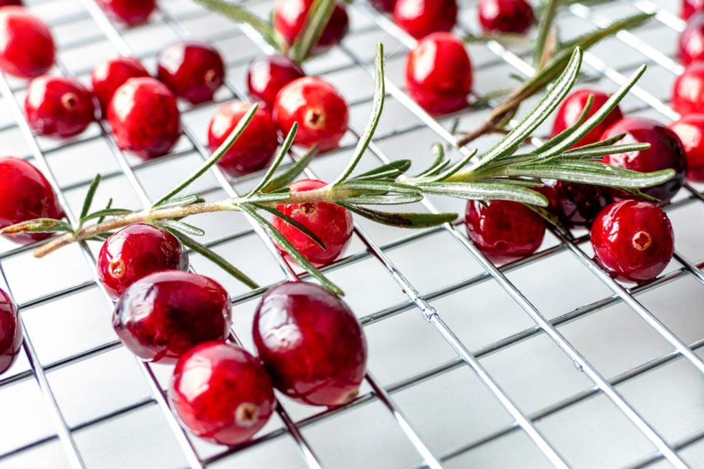 sugared cranberries and rosemary shown on a bed of white sugar