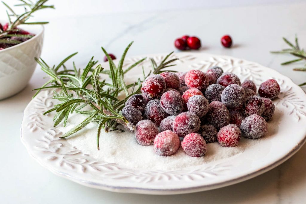 sugared cranberries and rosemary shown on a bed of white sugar