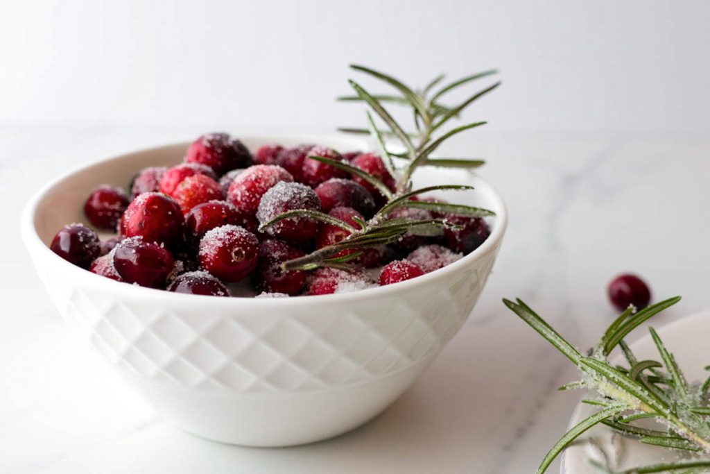 sugared cranberries and rosemary shown on a bed of white sugar