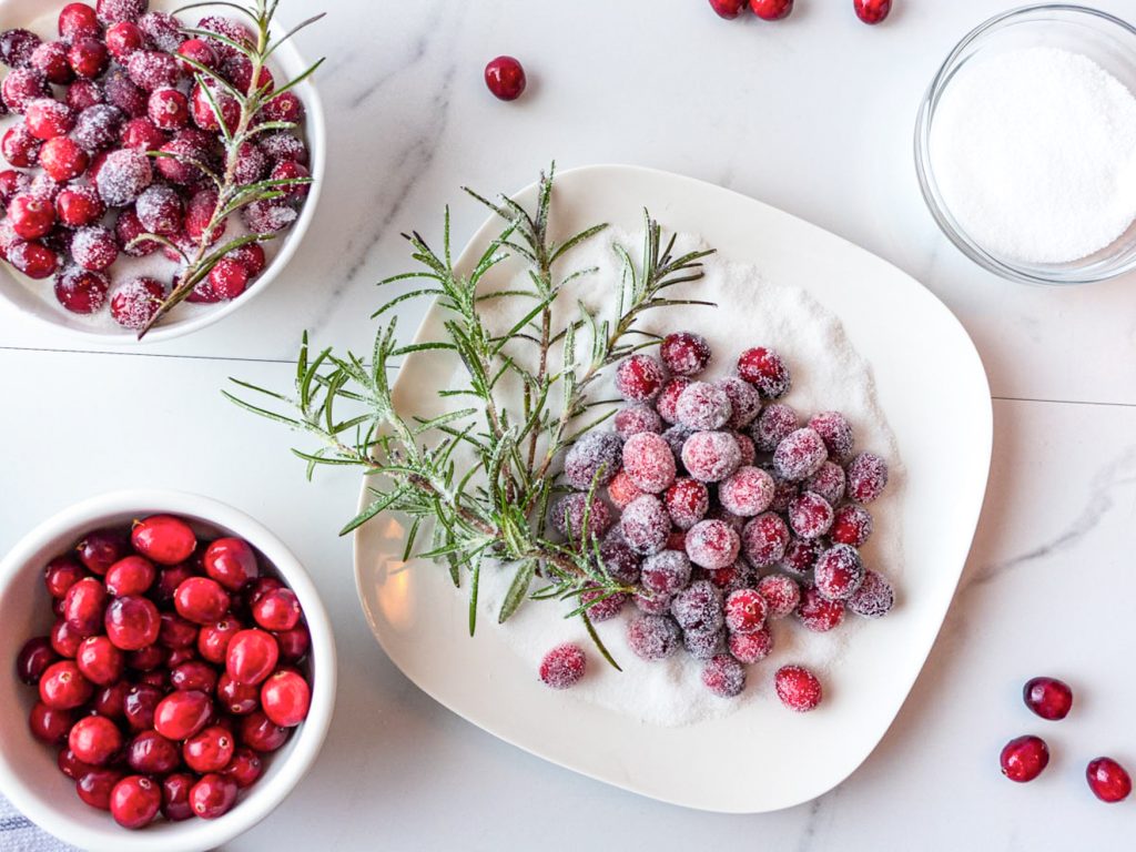 sugared cranberries and rosemary shown on a bed of white sugar