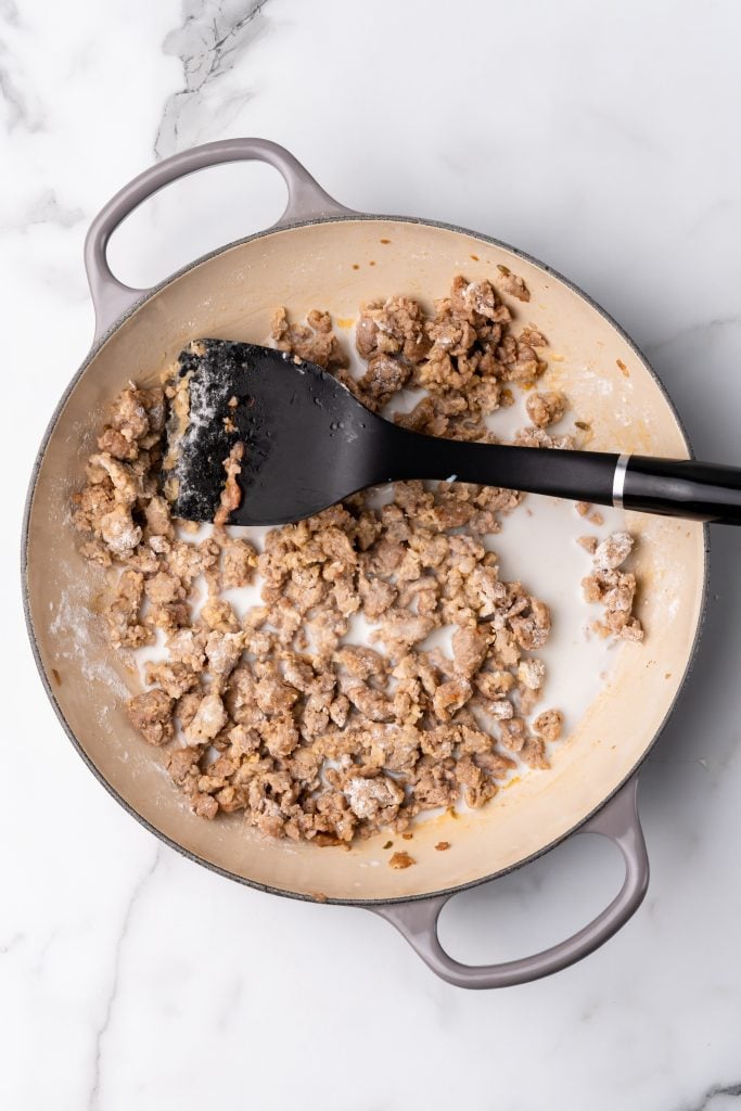 flour coated sausage crumbles in a large skillet with milk and a black spatula