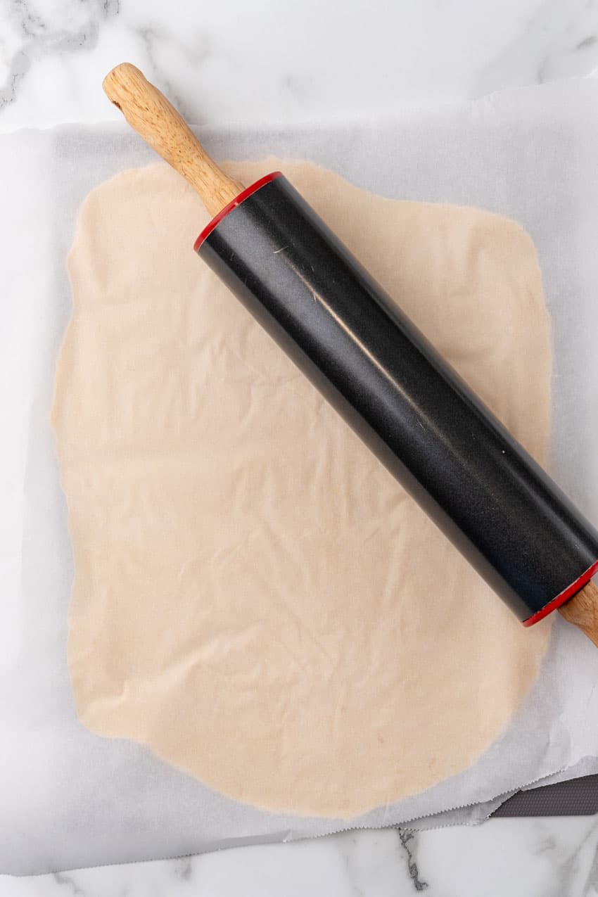 sugar cookie dough rolled out into a flat sheet between two pieces of wax paper