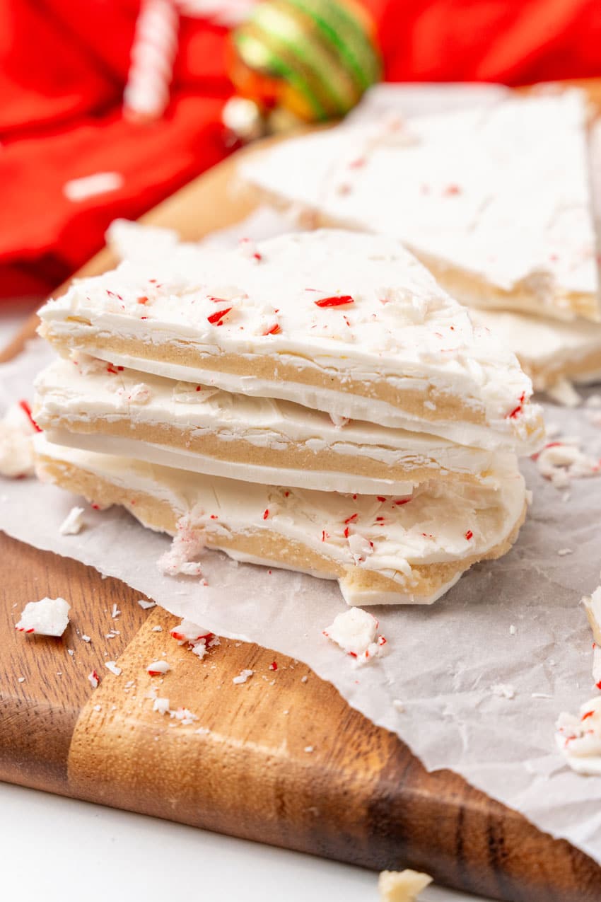 three pieces of peppermint sugar cookie bark stacked together on a parchment paper lined wooden cutting board