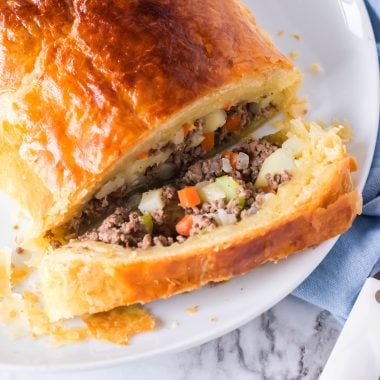sliced open golden brown ground beef filled wellington on a white platter