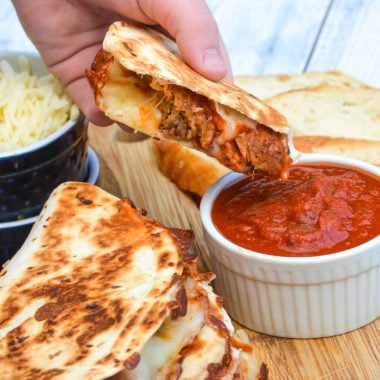 a hand dipping a sliced meatball quesadilla into a dipping bowl of marinara sauce