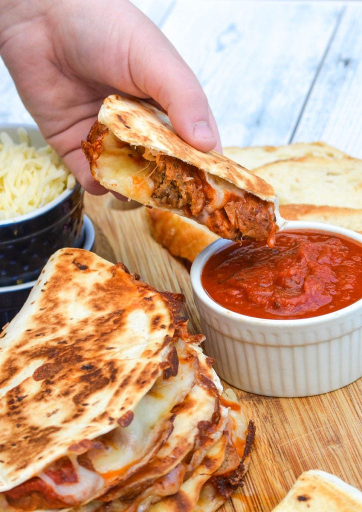 a hand dipping a sliced meatball quesadilla into a dipping bowl of marinara sauce