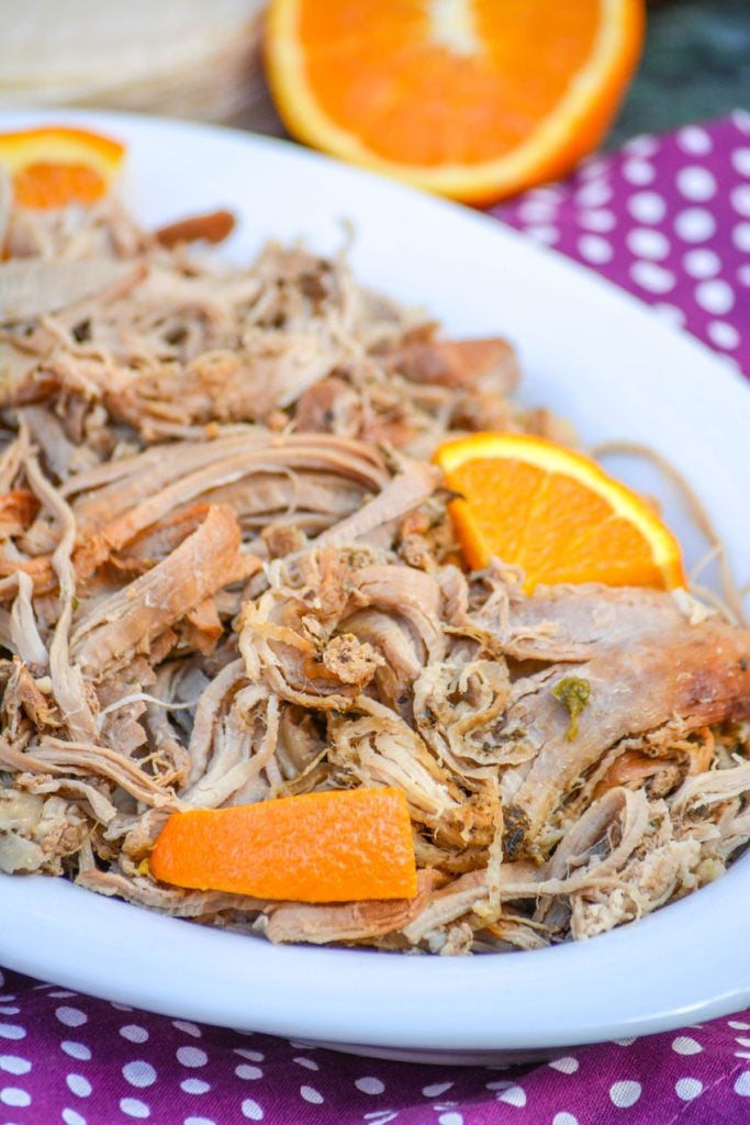 Crockpot Pork Carnitas with the shredded pork shown in a white serving dish and studded with fresh orange slices