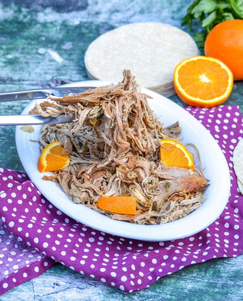 Crockpot Pork Carnitas with the shredded pork shown in a white serving dish and studded with fresh orange slices