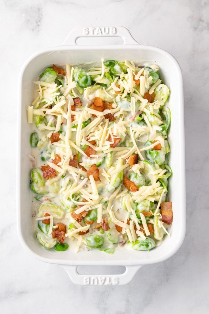 creamy burssels sprouts in a white casserole dish topped with bacon