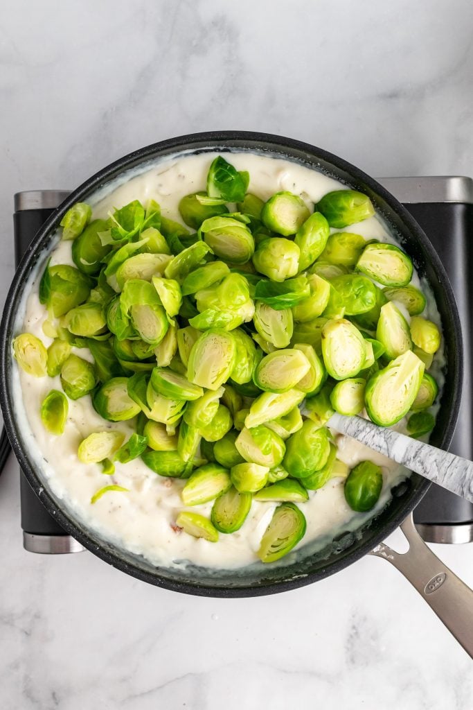 lightly steamed brussels sprouts being stirred into a skillet of white sauce for brussels sprout gratin casserole