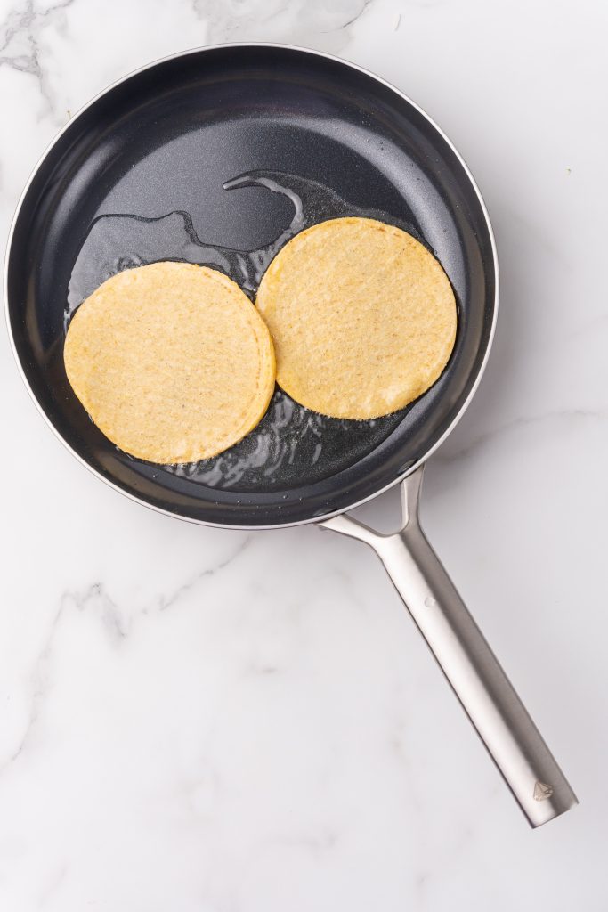 two corn tortillas in a skillet with hot oil
