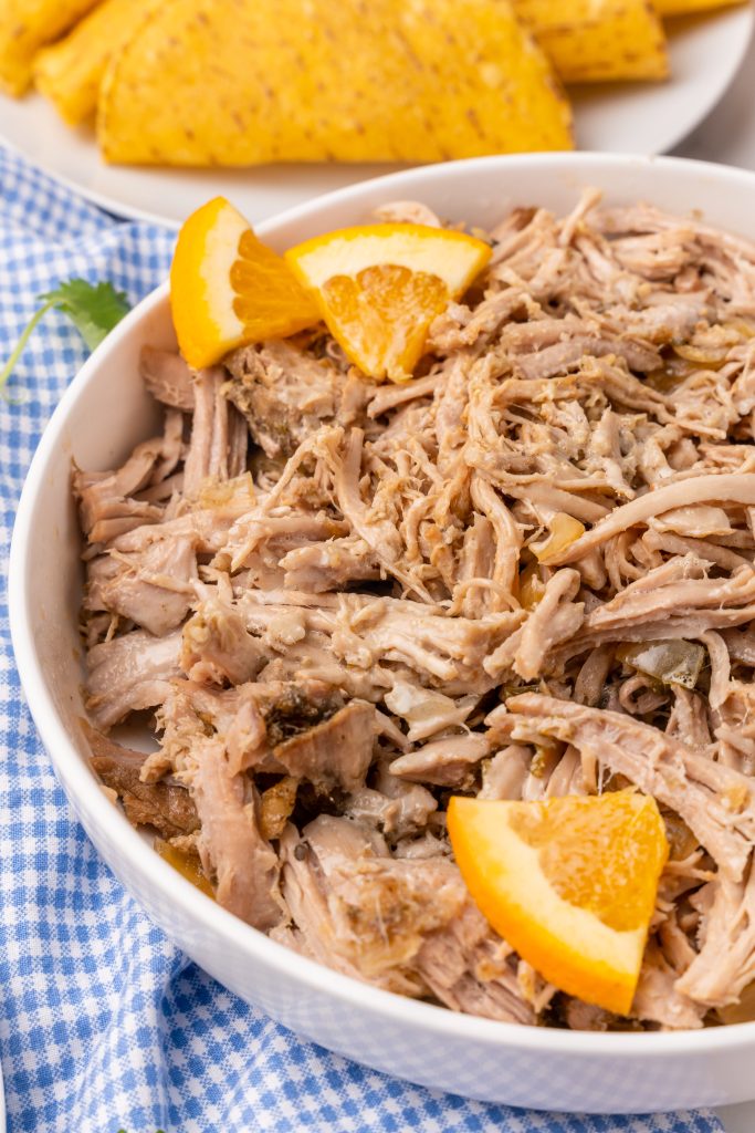pulled pork carnitas meat in a white serving bowl with quartered oranges