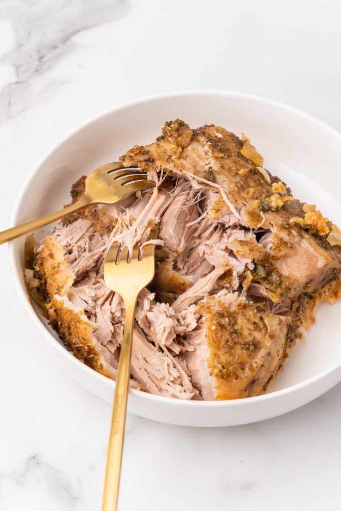 two gold forks pulling cooked pork in a white bowl
