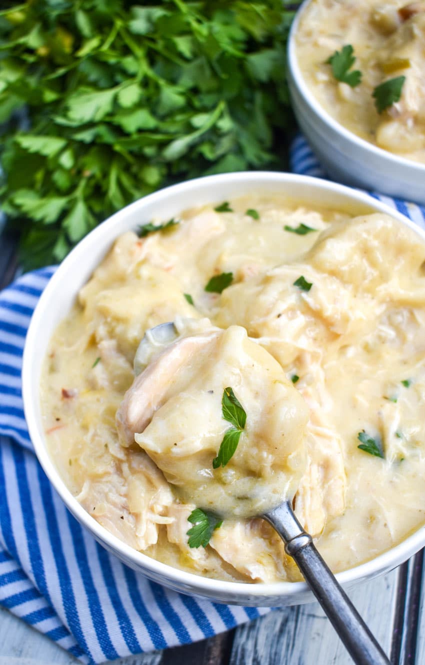 a spoon scooping crockpot chicken and dumplings out of a white soup bowl