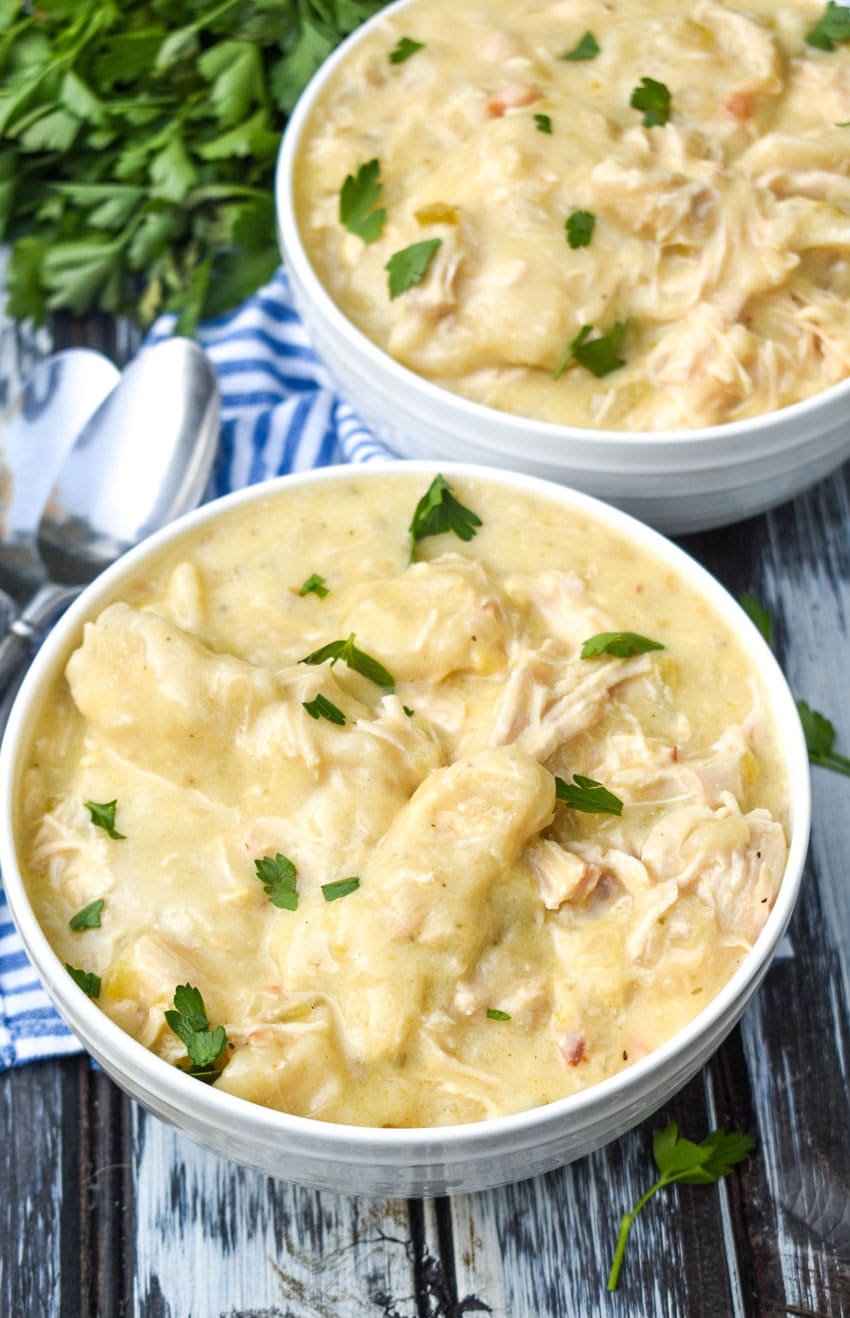 slow cooker chicken and dumplings topped with fresh parsley leaves in two white bowls