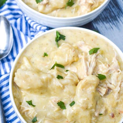 slow cooker chicken and dumplings topped with fresh parsley leaves in two white bowls