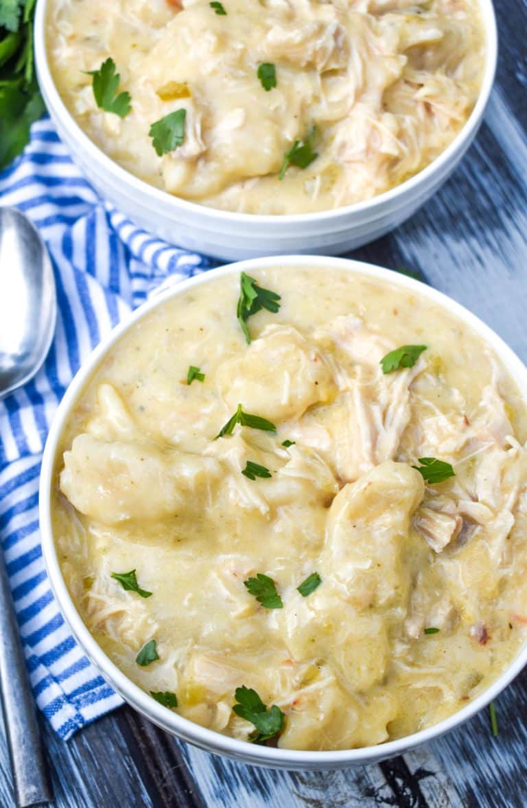 slow cooker chicken and dumplings topped with fresh parsley leaves in two white bowls